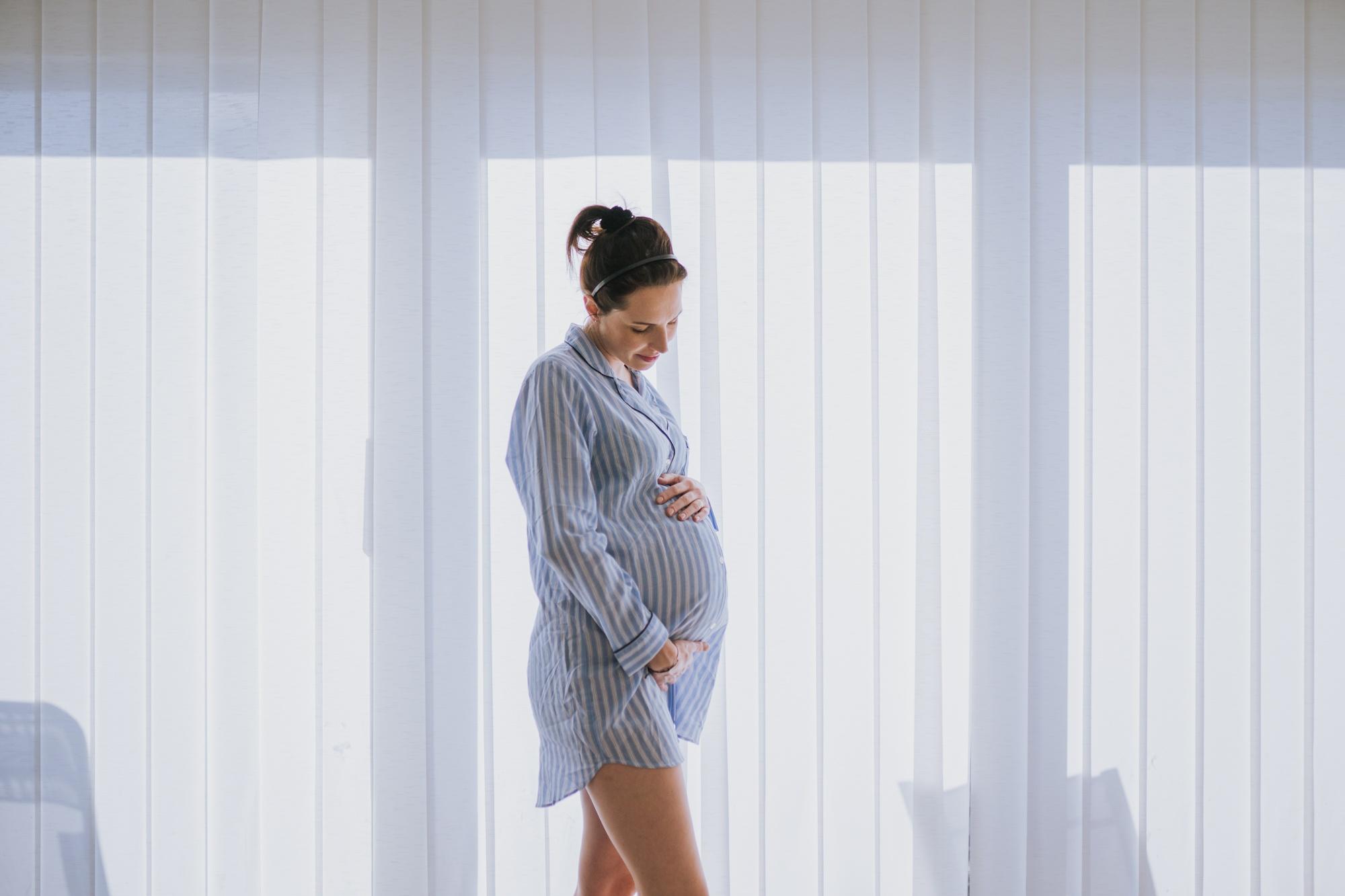 Pregnant woman standing, holding her hands on her belly.