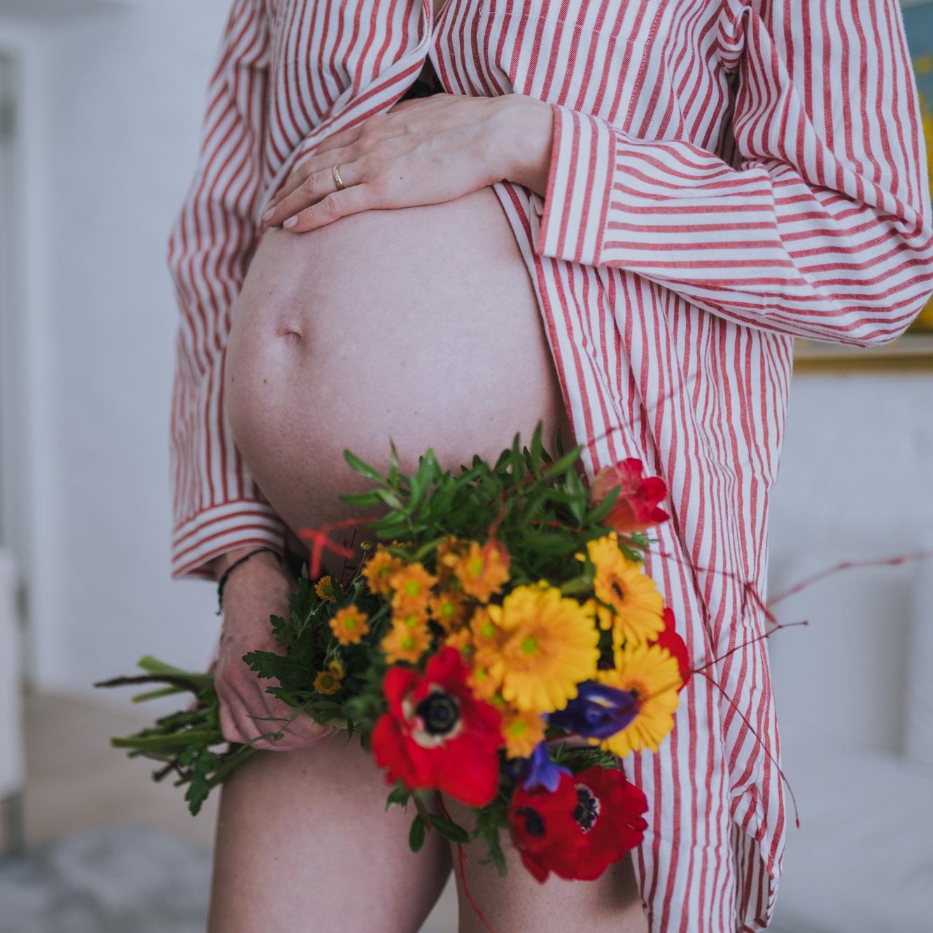 Pregnant woman, holding one hand on her large belly and the other holding a bouquet of flowers.