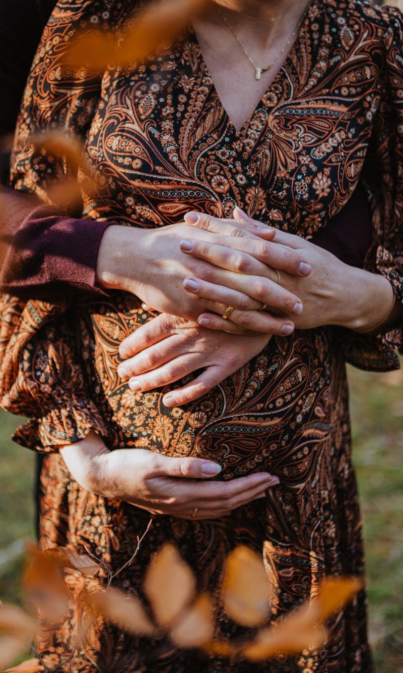 Pregnant woman and partner, both holding their hands on her baby bump.